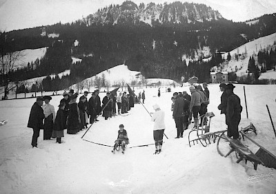 Ein Preisrodeln war die erste Sportveranstaltung, die von der jungen Wintersportvereinigung 1903 in Kitzbühel organisiert wurde. Das Foto zeigt das Ziel eines Rodelwettbewerbs im Jahr 1909. Erstmals wurde eine „elektrische“ Zeitnehmung eingesetzt. Gut erkennbar ist die „Schnur“ der Zeitmesser.